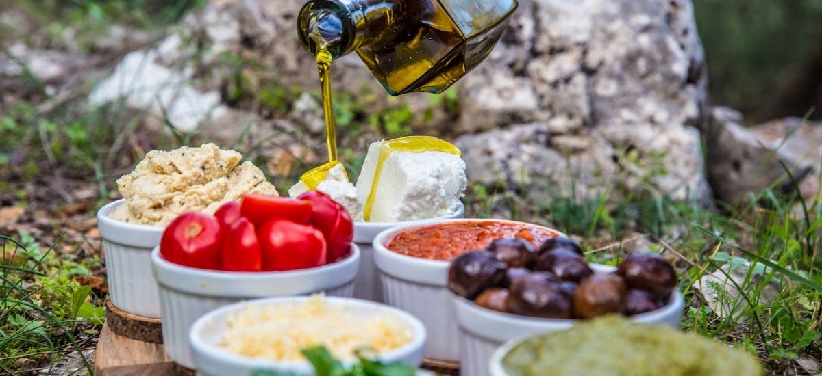 Outdoor picnic with various Mediterranean spreads, herbs, and olive oil drizzle.