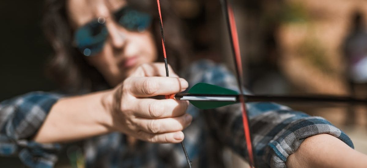 Close-up of an archer focusing intensely on aiming with a bow and arrow outdoors.