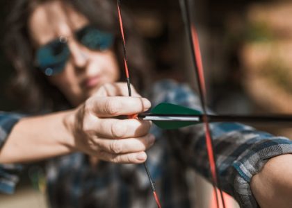 Close-up of an archer focusing intensely on aiming with a bow and arrow outdoors.